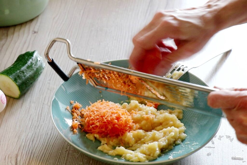 BLW Rezept Dinkelvollkorn Pancakes Frau reibt Karotte mit Gemüsereibe
