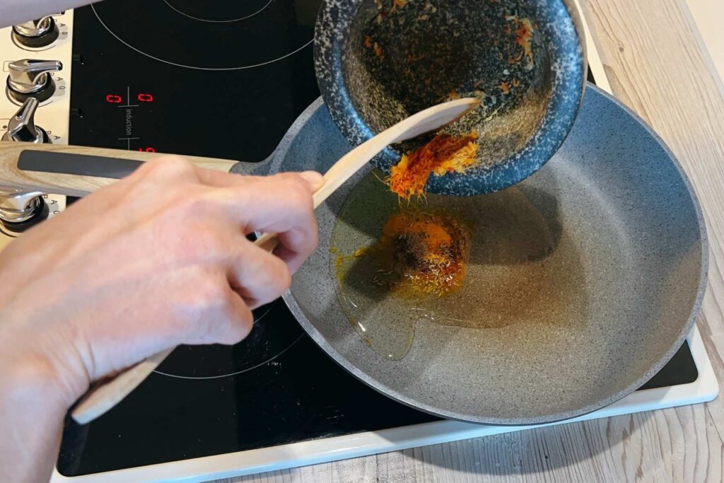 Frau fügt Ingwer und Chili zu den Gewürzen in der Pfanne für das Palak Paneer hinzu